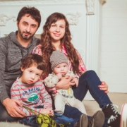 A white couple sits on the floor smiling with two small children in their laps.