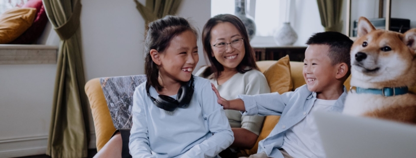 An Asian woman and two young children are smiling and playing on a yellow couch.