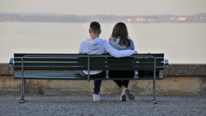 A couple sitting on a bench from behind, facing a body of water.