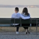 A couple sitting on a bench from behind, facing a body of water.