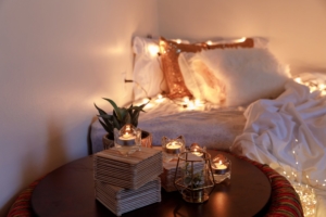 A photo of a cozy bedroom, with twinkle lights, soft bedding, and candles glowing.