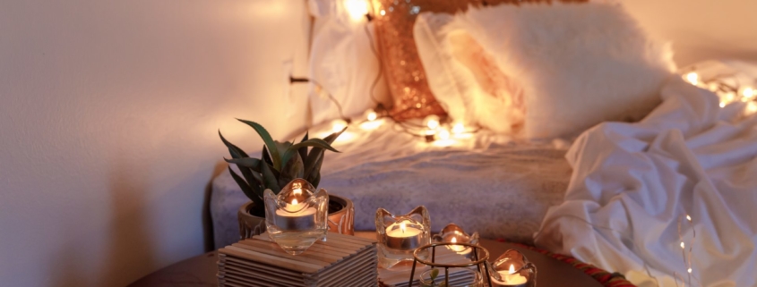 A photo of a cozy bedroom, with twinkle lights, soft bedding, and candles glowing.