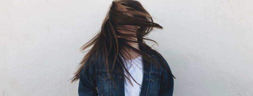 A stock photo of a woman with long dark hair standing in gray fog, tossing her head so her hair covers her face.
