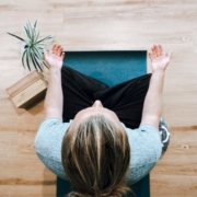 A white woman sitting on a yoga mat spread out on a hardwood floor, taken from above.