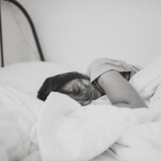 A black and white photo of a woman sleeping in a bed with white linens.