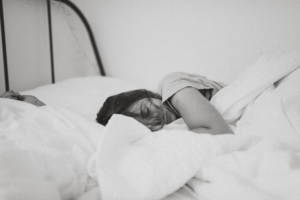 A black and white photo of a woman sleeping in a bed with white linens. 