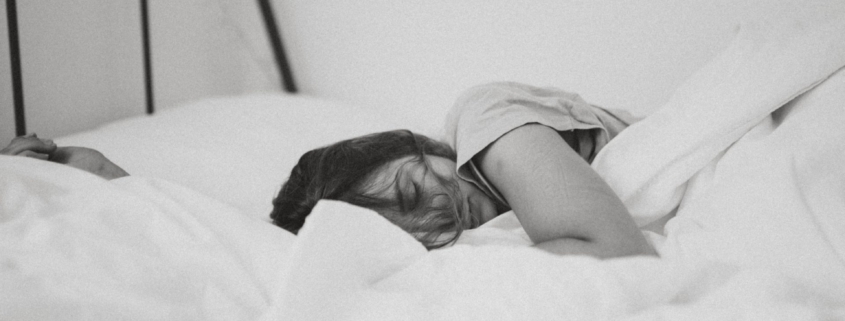 A black and white photo of a woman sleeping in a bed with white linens.