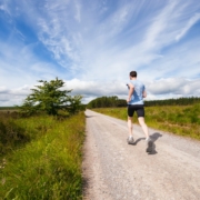 A stock photo of a man running on an unpaved path outisde under a blue sky.