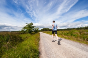 A stock photo of a man running on an unpaved path outisde under a blue sky. 