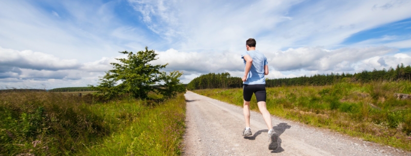 A stock photo of a man running on an unpaved path outisde under a blue sky.