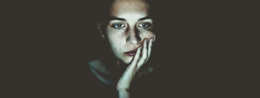 A stock photo of a woman in a dark room with her face lit up by a screen.