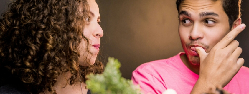 A man and a woman eating and looking at one another.