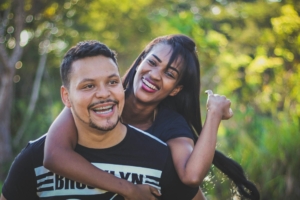 A woman standing behind a man, with her arms around him, and both are smiling.