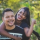 A woman standing behind a man, with her arms around him, and both are smiling.