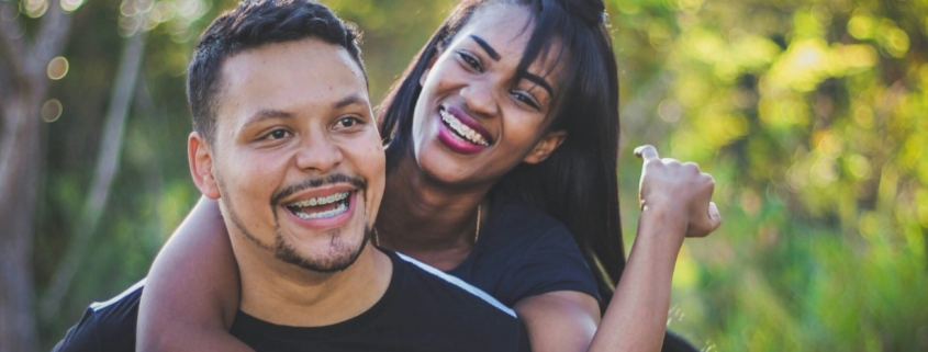 A woman standing behind a man, with her arms around him, and both are smiling.