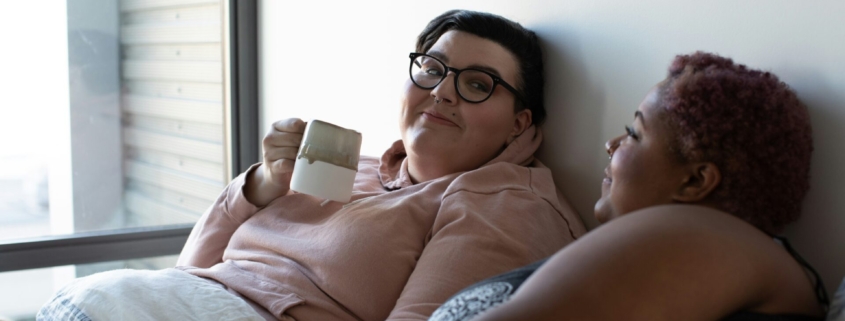 Two plus size women drinking coffee in bed together.