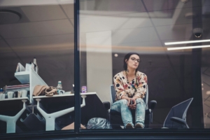 A woman in an office sitting in front of a window looking thoughtful.