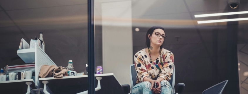 A woman in an office sitting in front of a window looking thoughtful.