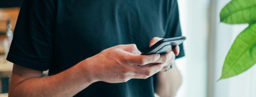 A man from the neck down, typing on a phone.