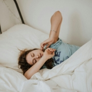 A woman stretching in a bed made up with white linens.