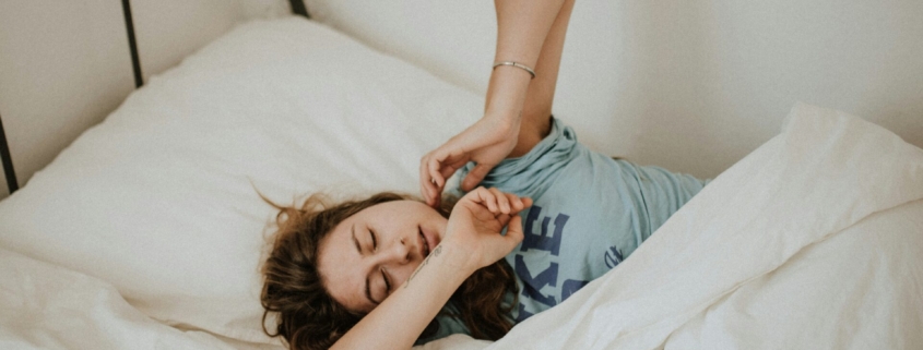 A woman stretching in a bed made up with white linens.