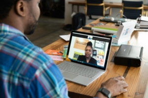 A photo showing a Black man sitting at a table having a video call with a Black woman. 