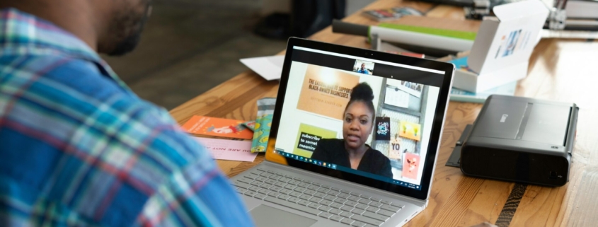 A photo showing a Black man sitting at a table having a video call with a Black woman.