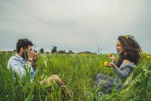 A man and a woman taking pictures in a field with flowers.