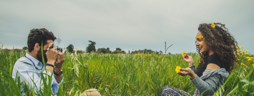 A man and a woman taking pictures in a field with flowers.