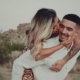 A heterosexual couple in a desert landscape, with the woman riding on the man's back. They're looking at each other affectionately.