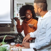 A Black couple cooking together and smiling in a kitchen.