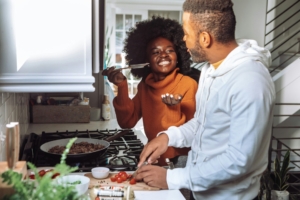 A Black couple cooking together and smiling in a kitchen.