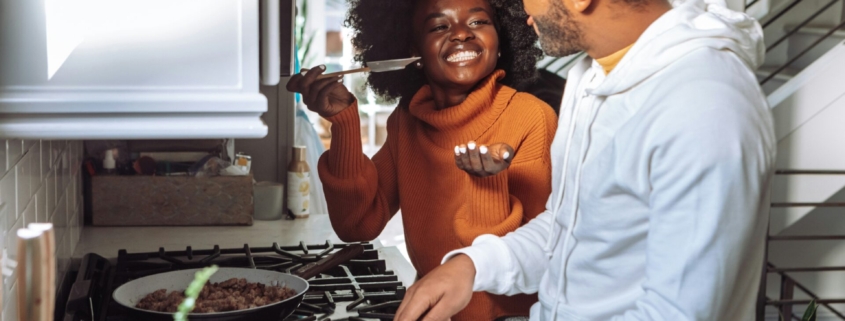 A Black couple cooking together and smiling in a kitchen.