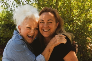 A stock photo of a middle aged white woman and an older white woman embracing outside.