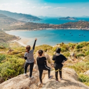 A group of women from above, standing on a rocky overlook with water in the distance.