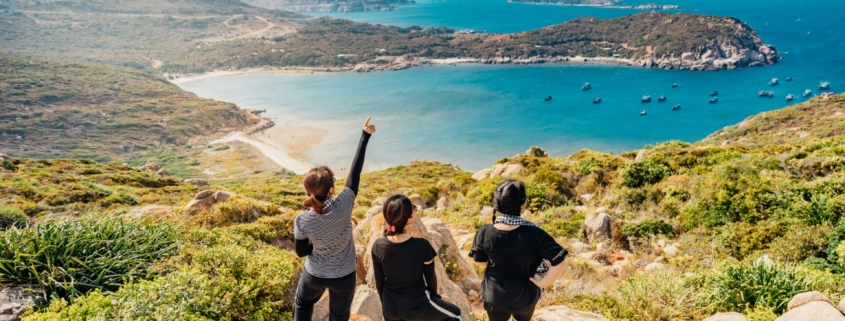 A group of women from above, standing on a rocky overlook with water in the distance.