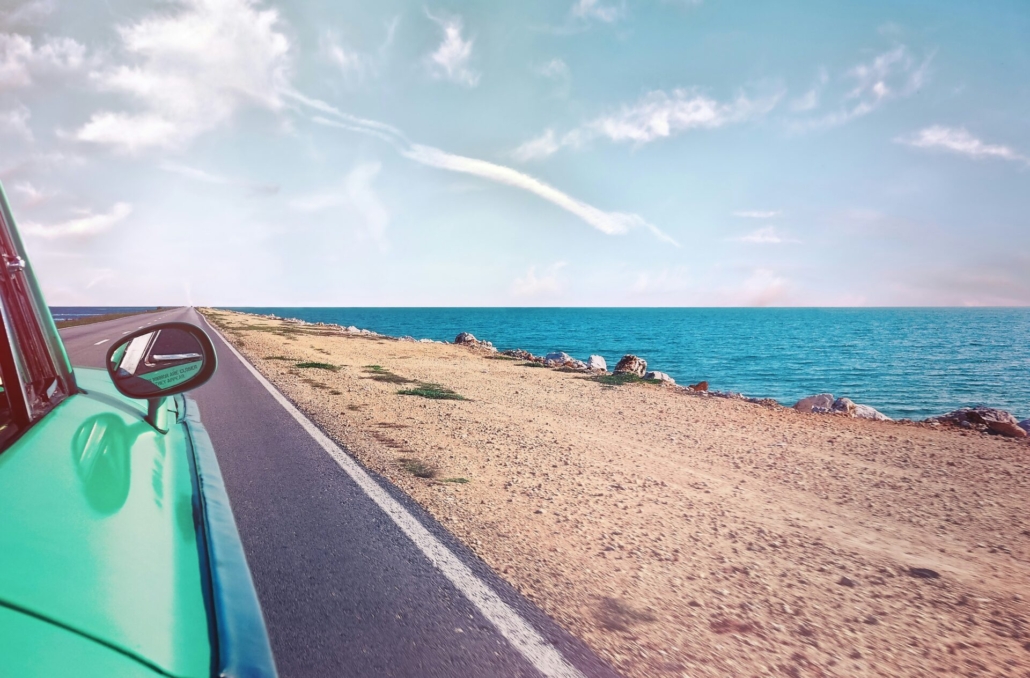 A photo of a beach on a sunny day taken from the window of a car.