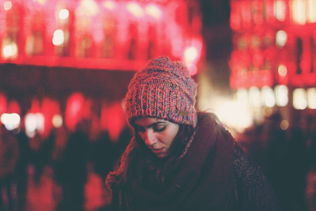 A woman walking outside in a busy area, wearing a winter coat and hat.