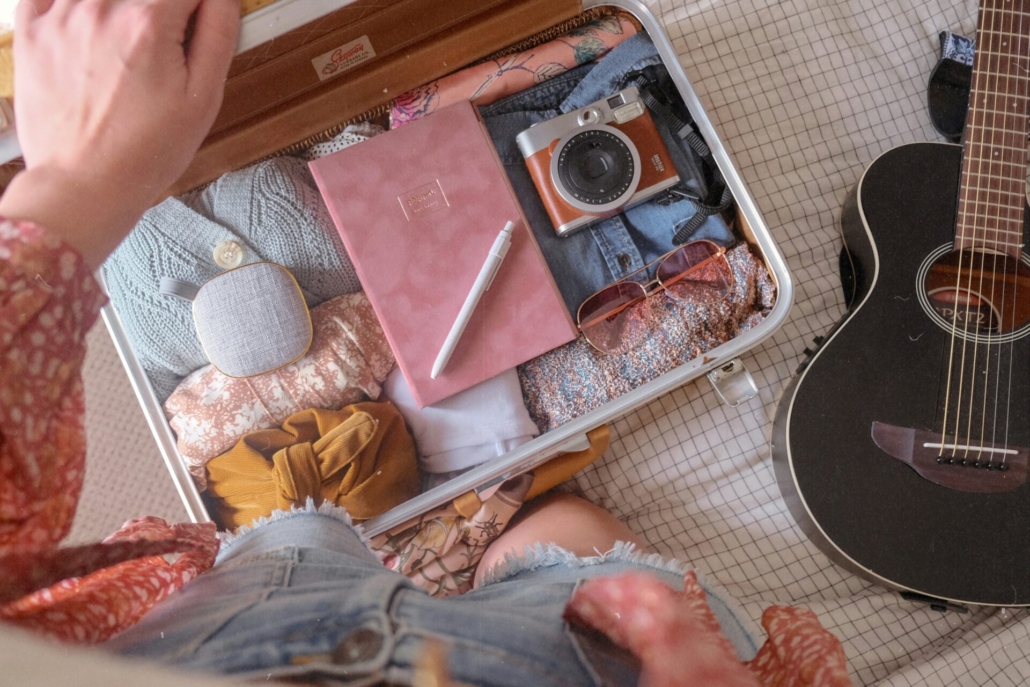 A person standing over a packed suitcase lying on a bed, next to a guitar.