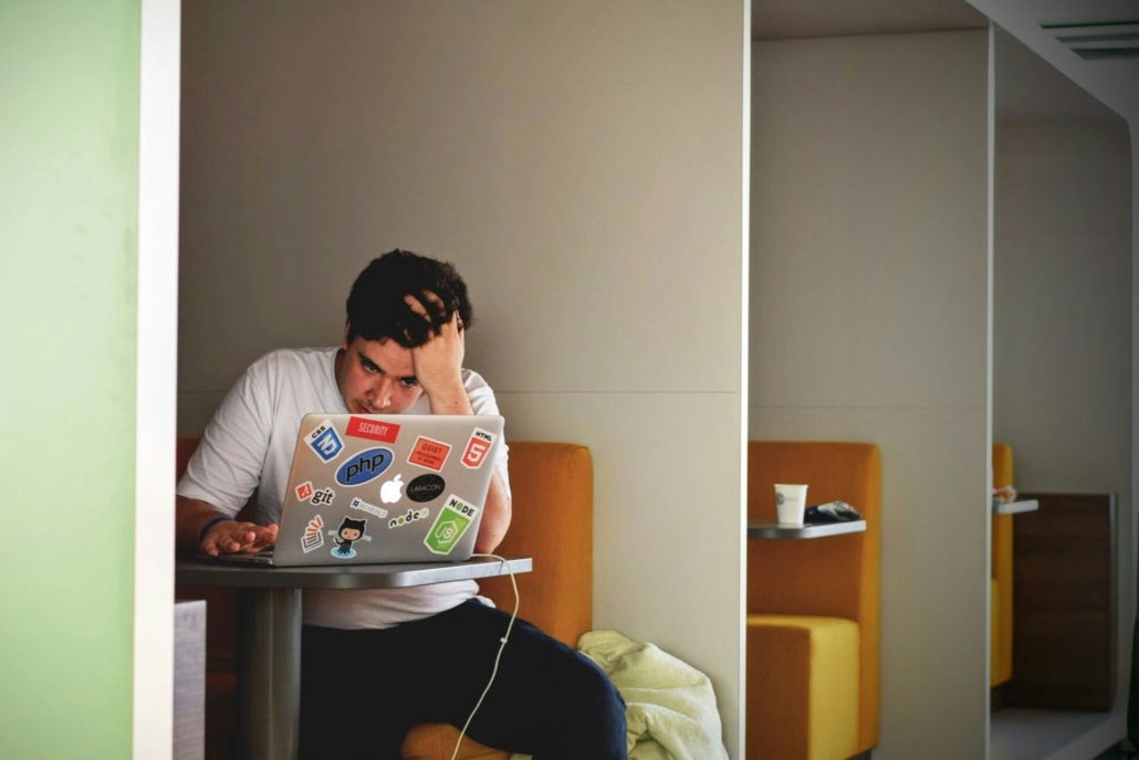 A stressed looking man sitting in an alcove in front of a laptop.