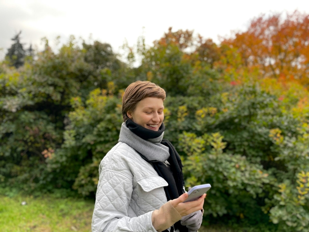 A person standing outside, looking at a phone and smiling.