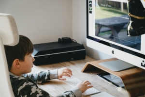 An elementary school age Asian boy sitting at a desk using a desktop computer.