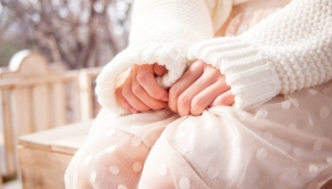 A person wearing all white, from the chest down, with their hands on their lap.