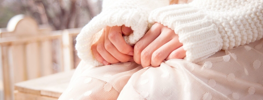 A person wearing all white, from the chest down, with their hands on their lap.