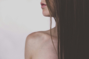 The bare shoulder and lower face of a person with long dark hair.