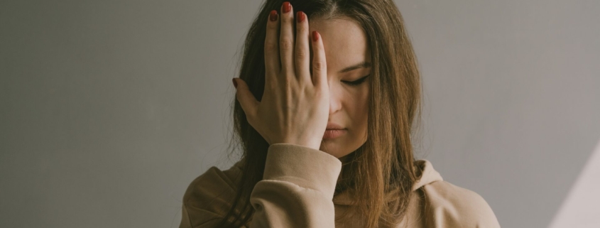 A white woman with her hand on her forehead, looking frustrated.