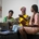 A group of Black women sitting on a couch, talking. They are holding notebooks and there is a computer on the table in front of them.