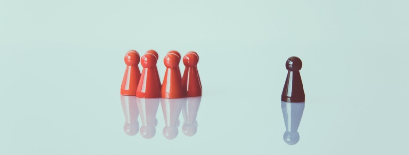 A light blue graphic showing a group of four red figurines grouped on the left side of the photo, and a black figurine alone on the right side.