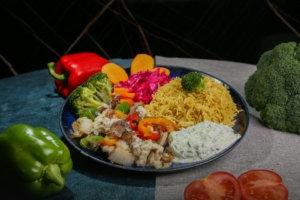 A plate of food including cooked vegetables and rice, with whole vegetables on the table surrounding the plate.