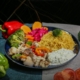 A plate of food including cooked vegetables and rice, with whole vegetables on the table surrounding the plate.